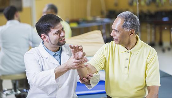 A doctor examines an older male patient's wrist.